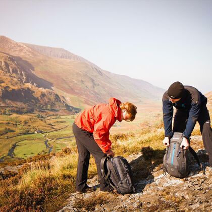 A young couple hiking in the Welsh mountains, arranging their backpacks.